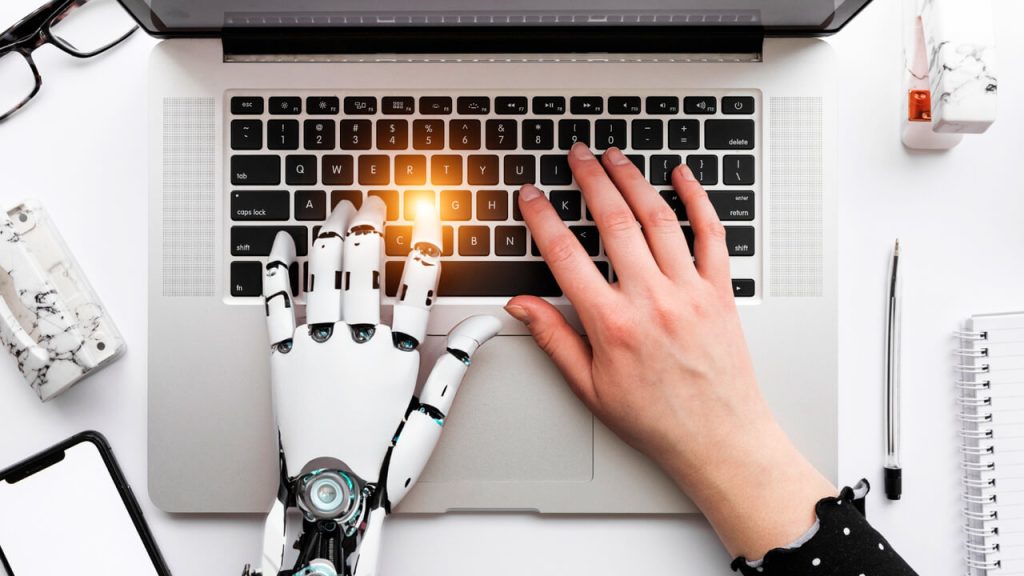 main humaine et main robotique sur un clavier d'ordinateur